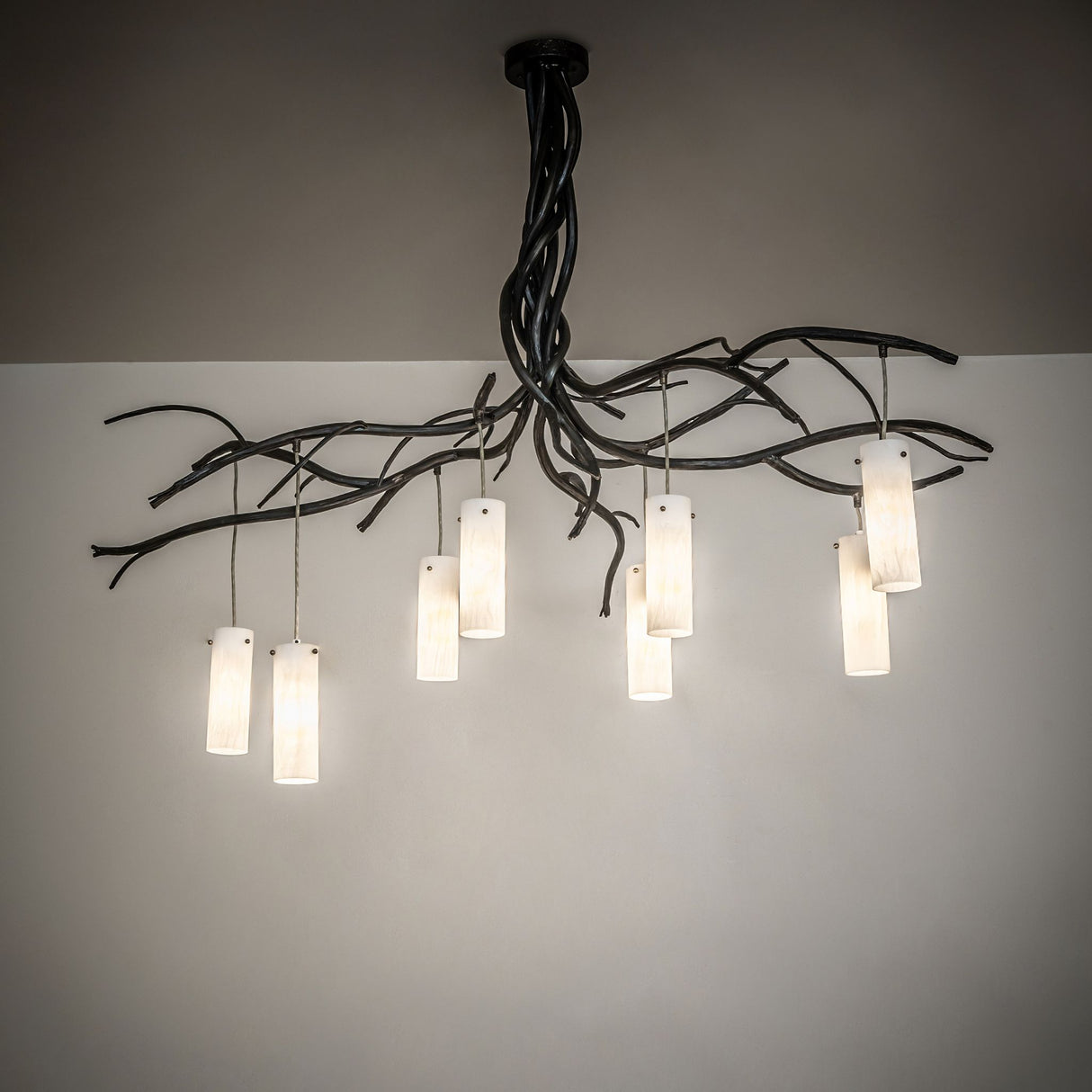 Ambient room view of the chandelier casting soft, warm light from cylindrical glass shades.